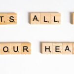 Wooden Scrabble tiles arranged to spell 'ITS ALL IN YOUR HEAD' on a white background.