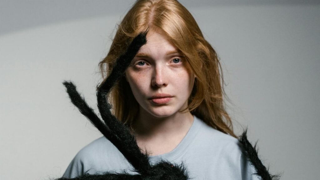 A young woman faces fear head-on, confronting an oversized spider calmly.