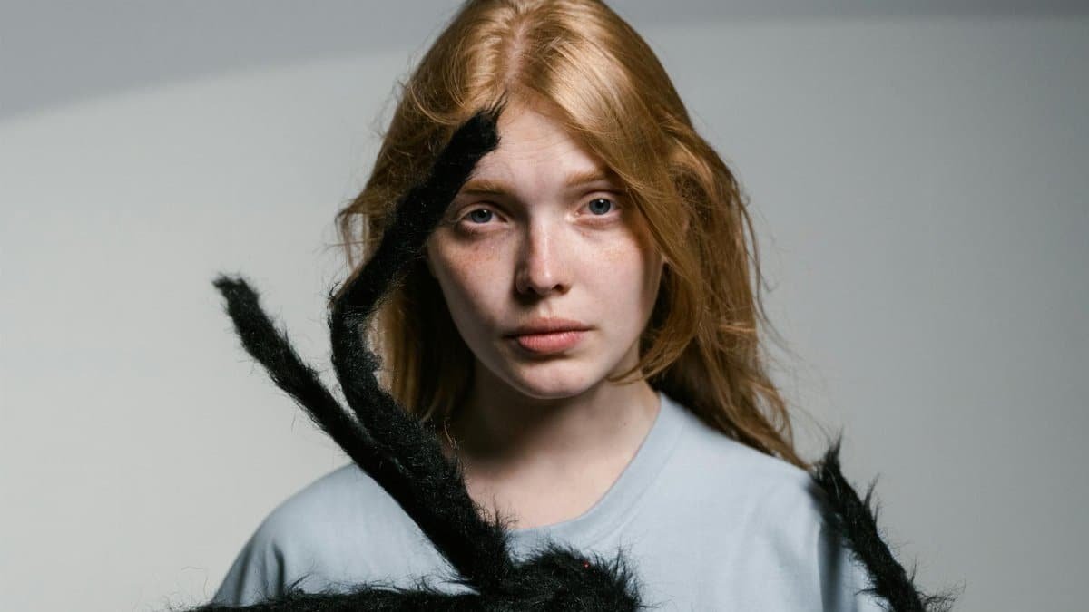A young woman faces fear head-on, confronting an oversized spider calmly.