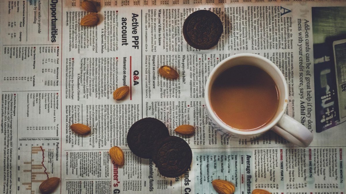 A cozy setup with coffee, cookies, and almonds on a newspaper, perfect for breakfast vibes.
