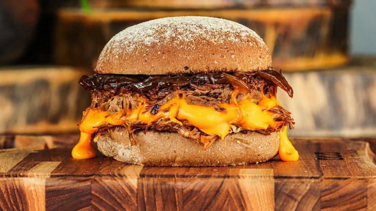 Delicious pulled pork burger with melted cheese on a wooden board.