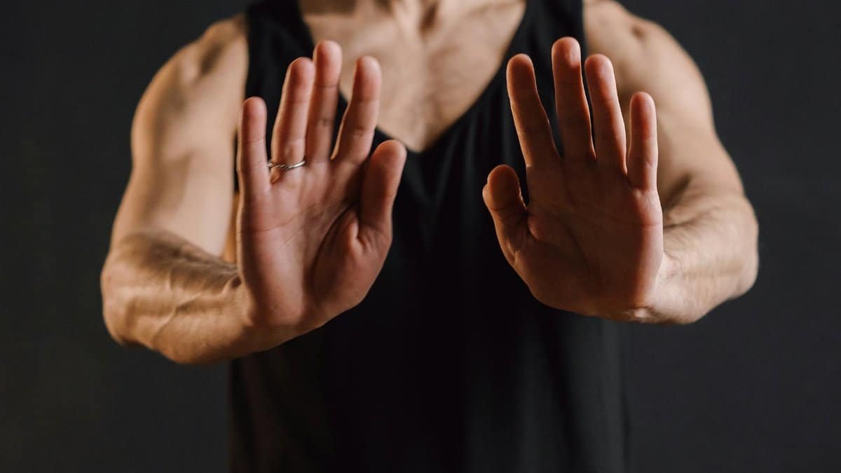 A focused close-up of a man in a black tank top performing a meditation gesture, hands in mudra.