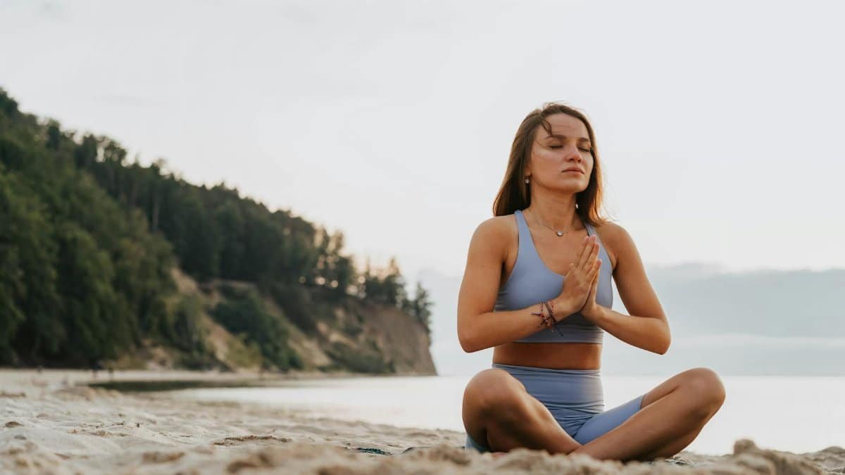 Woman practicing yoga meditation on a serene beach morning, promoting wellness.