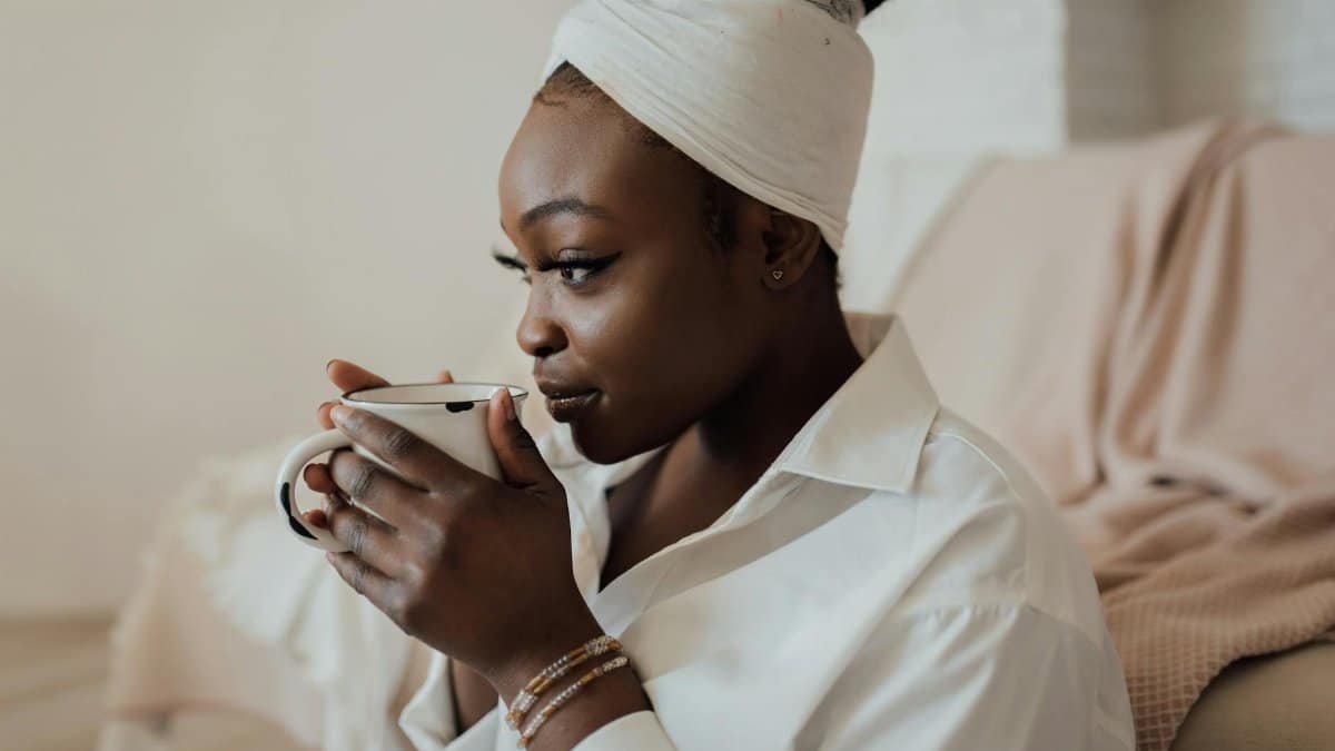 Woman with headwrap sipping coffee in cozy interior, reflecting relaxation lifestyle.