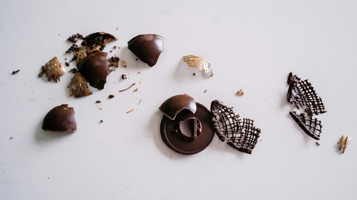 Close-up of broken dark chocolate pieces scattered across a smooth white surface. Ideal for food photography and dessert themes.