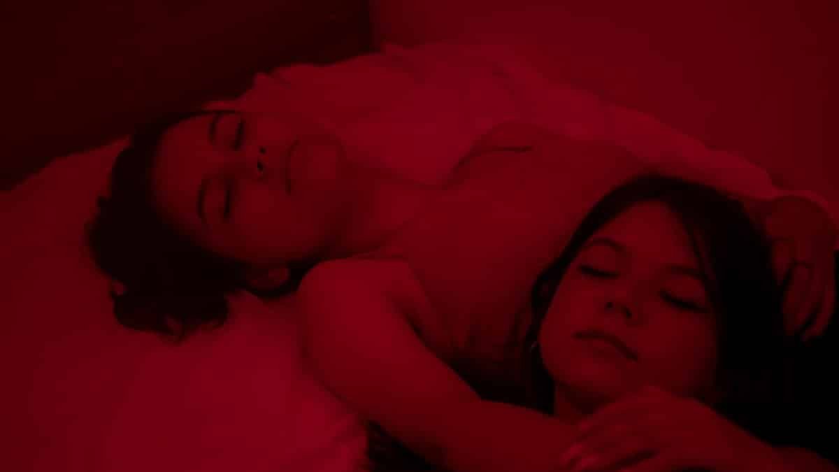 Two women lying in bed under a soothing red light, embracing tranquility.
