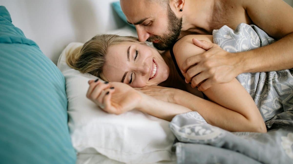 Happy couple embracing in bed, showcasing love and affection in a cozy home setting.