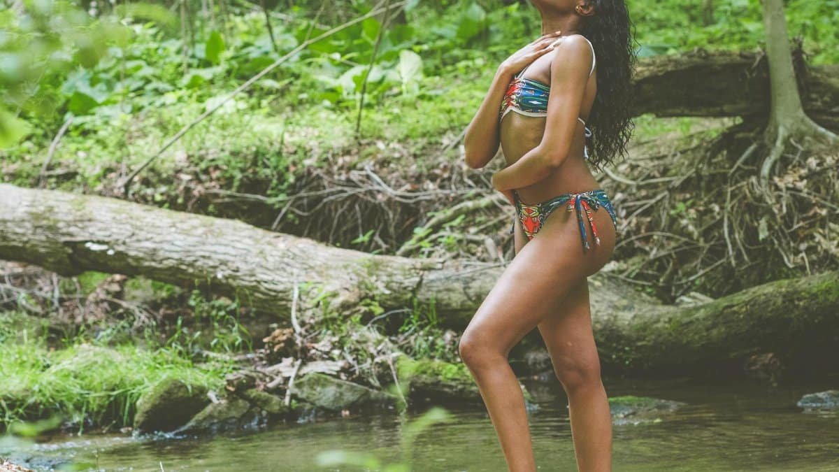 Young woman enjoying a tranquil moment by a forest stream, embodying summer relaxation and natural beauty.