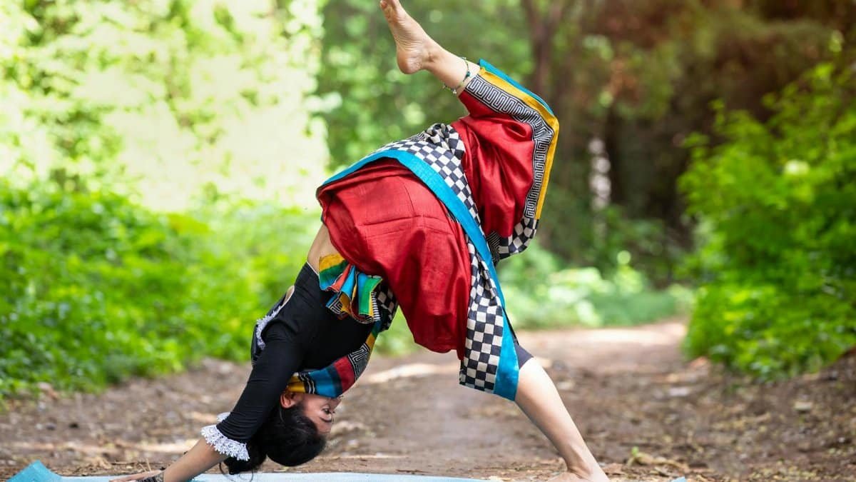 Woman practicing yoga outdoors in vibrant traditional clothing, showcasing flexibility and harmony with nature.