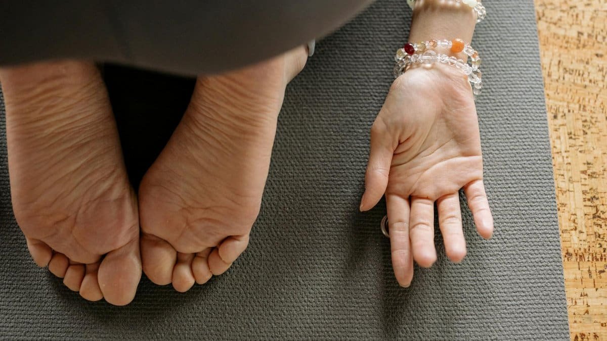 Feet and hand of a woman on yoga mat, showing bracelets and jewelry during exercise.