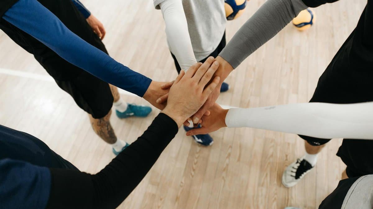 Close-up of athletes joining hands in a motivational sports huddle on an indoor court.