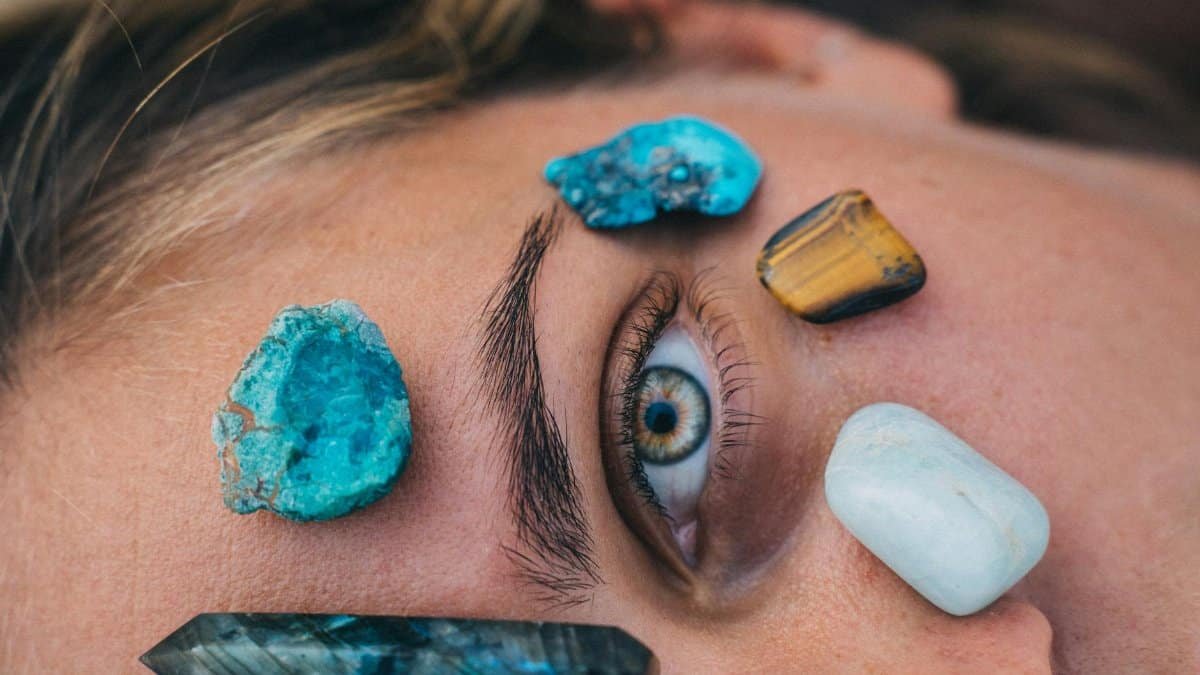 Close-up of a person's eye surrounded by vibrant healing stones on skin for relaxation therapy.