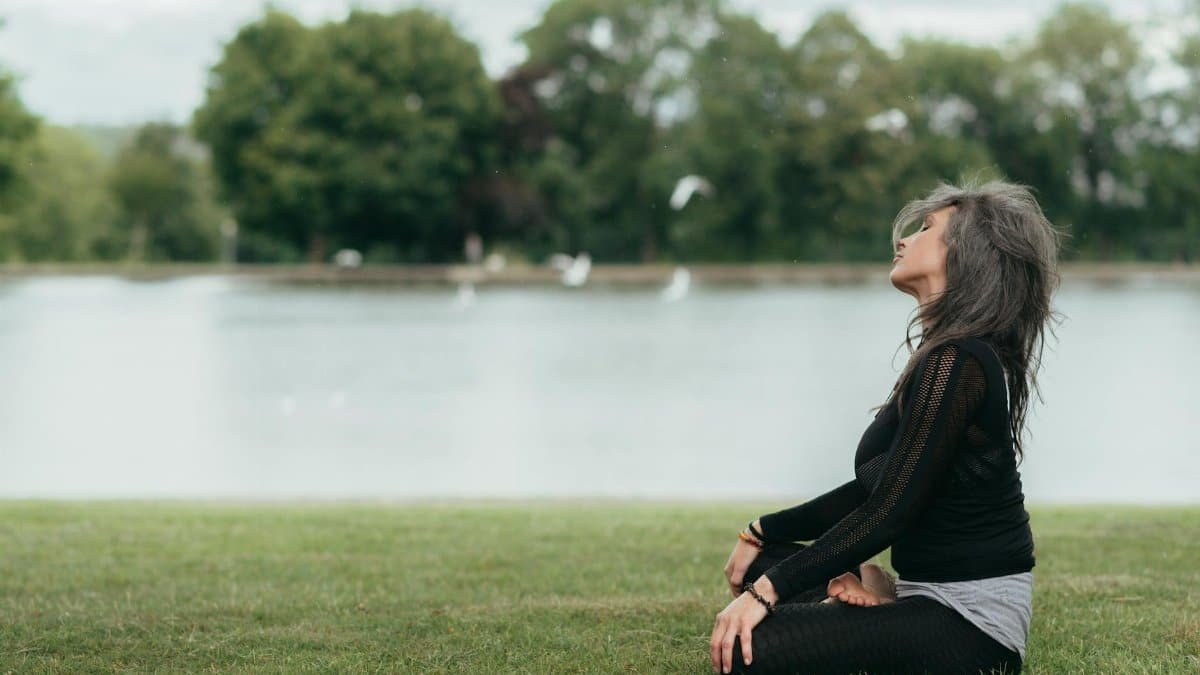 Woman practicing yoga meditation by a tranquil lake, embracing mindfulness and peace.