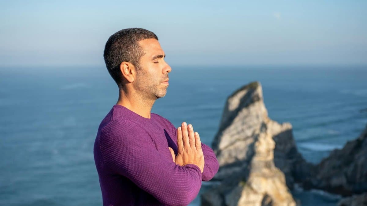 Side view of a man meditating by the ocean cliffs in Portugal, promoting relaxation and mindfulness.