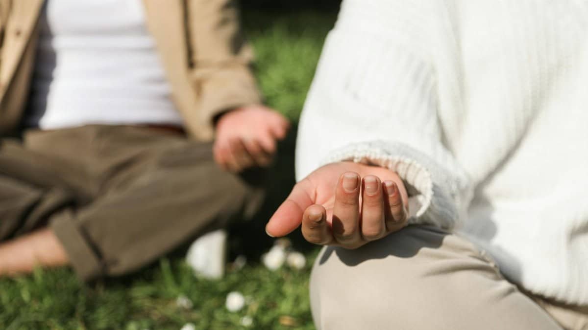 Two people meditating outdoors, focusing on hands in a peaceful setting.