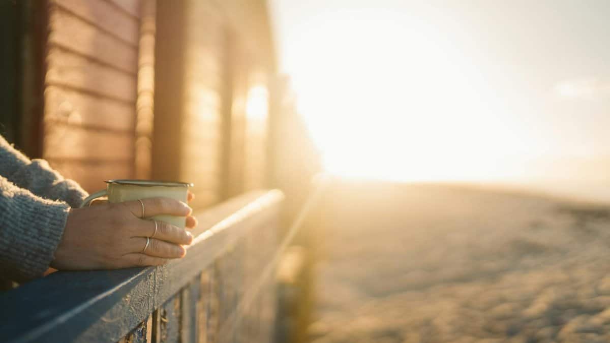 A serene morning scene with a hand holding a mug at sunrise, capturing warmth and tranquility.