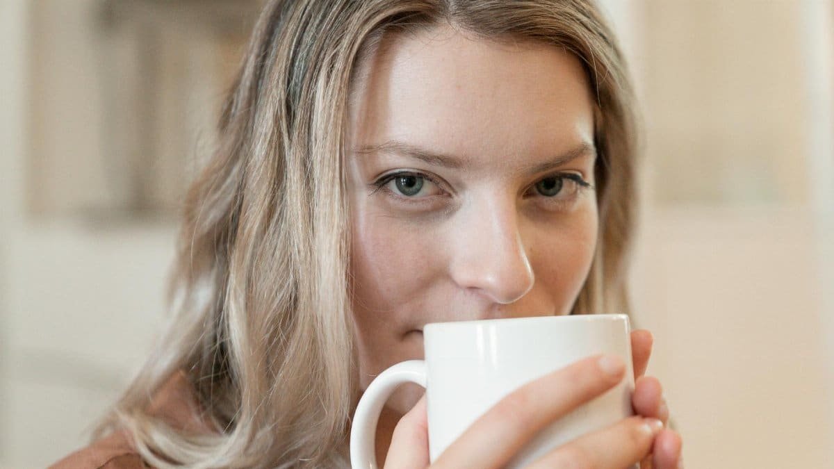 Close-up of a young woman enjoying a warm drink indoors, promoting relaxation.