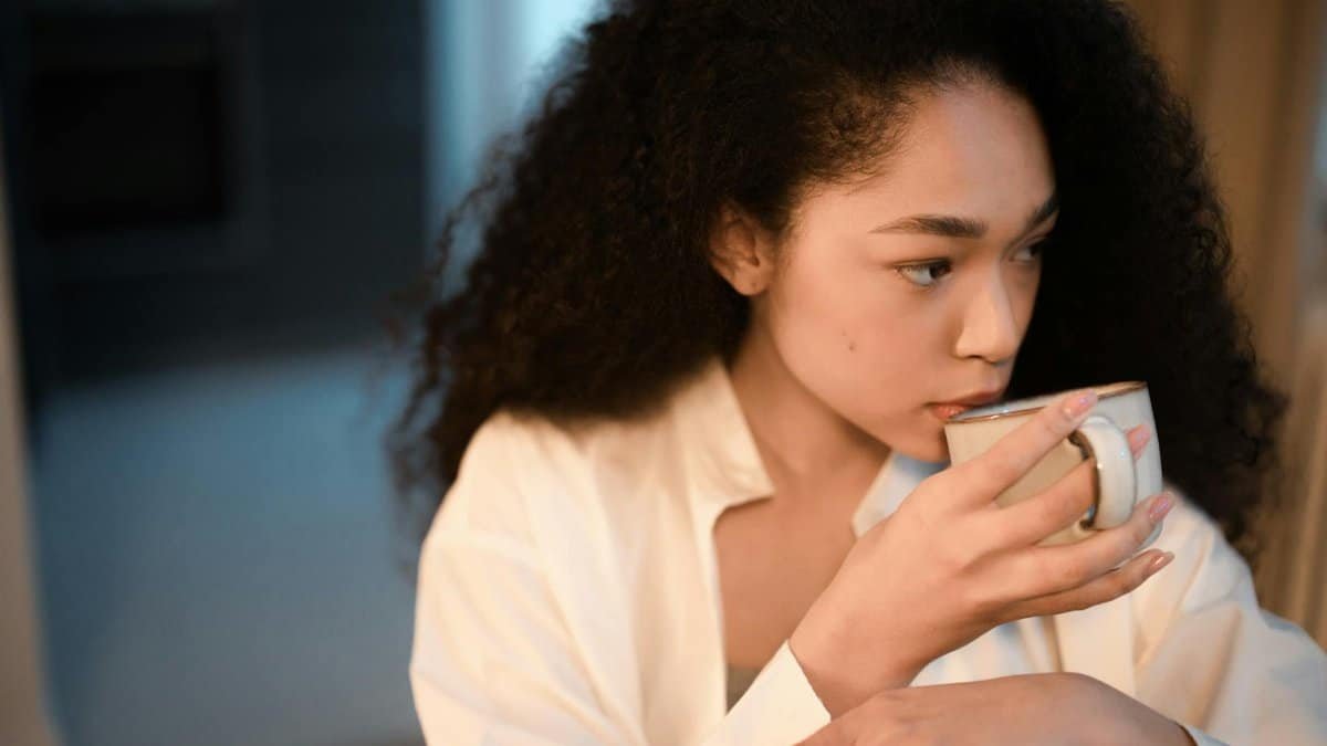 A woman with curly hair savoring a cup of coffee indoors, embracing a peaceful morning atmosphere.