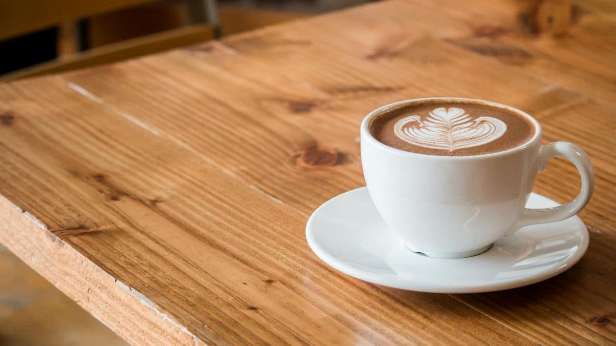 Close-up of a white cup of latte with artistic foam on a rustic wooden table.
