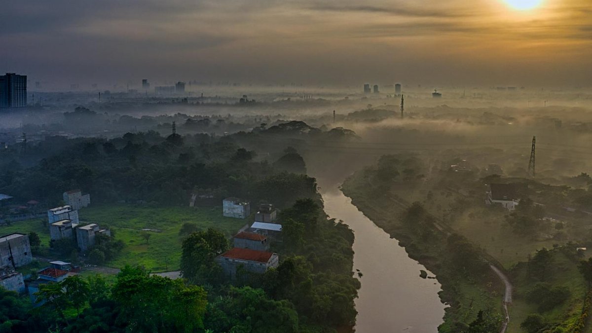 Aerial view of a serene river winding through lush greenery and misty morning landscape in Banten, Indonesia.