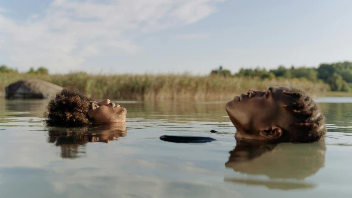 Two men floating peacefully in a calm lake with reflections on a sunny day.