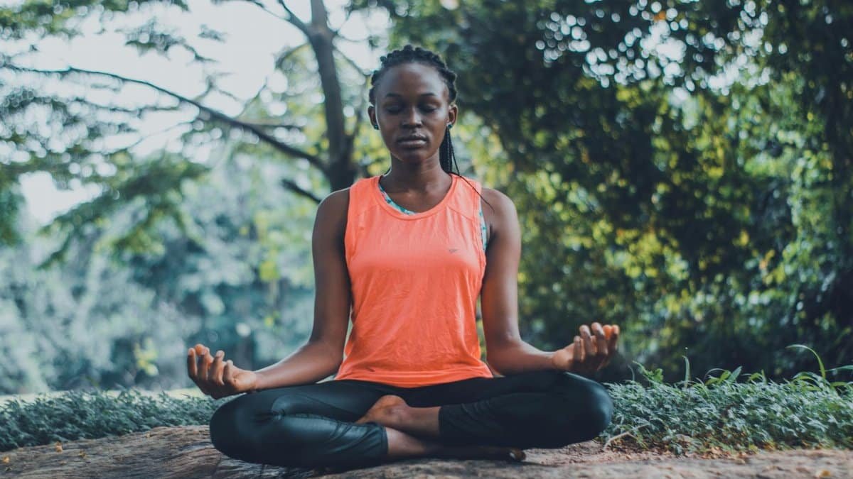 A woman meditating peacefully outdoors in a lush green setting, promoting relaxation and mindfulness.
