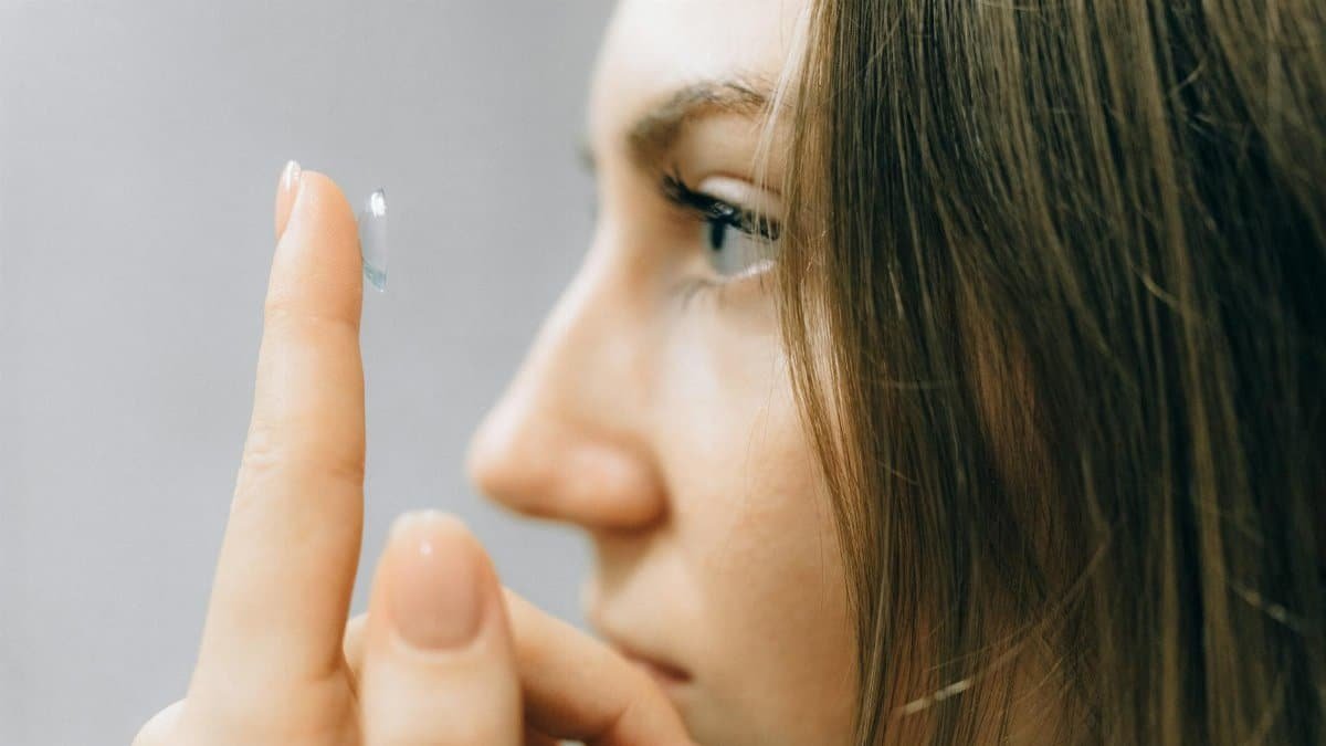 A young woman focuses intently as she applies a contact lens, close-up shot highlighting her eye and careful fingers.