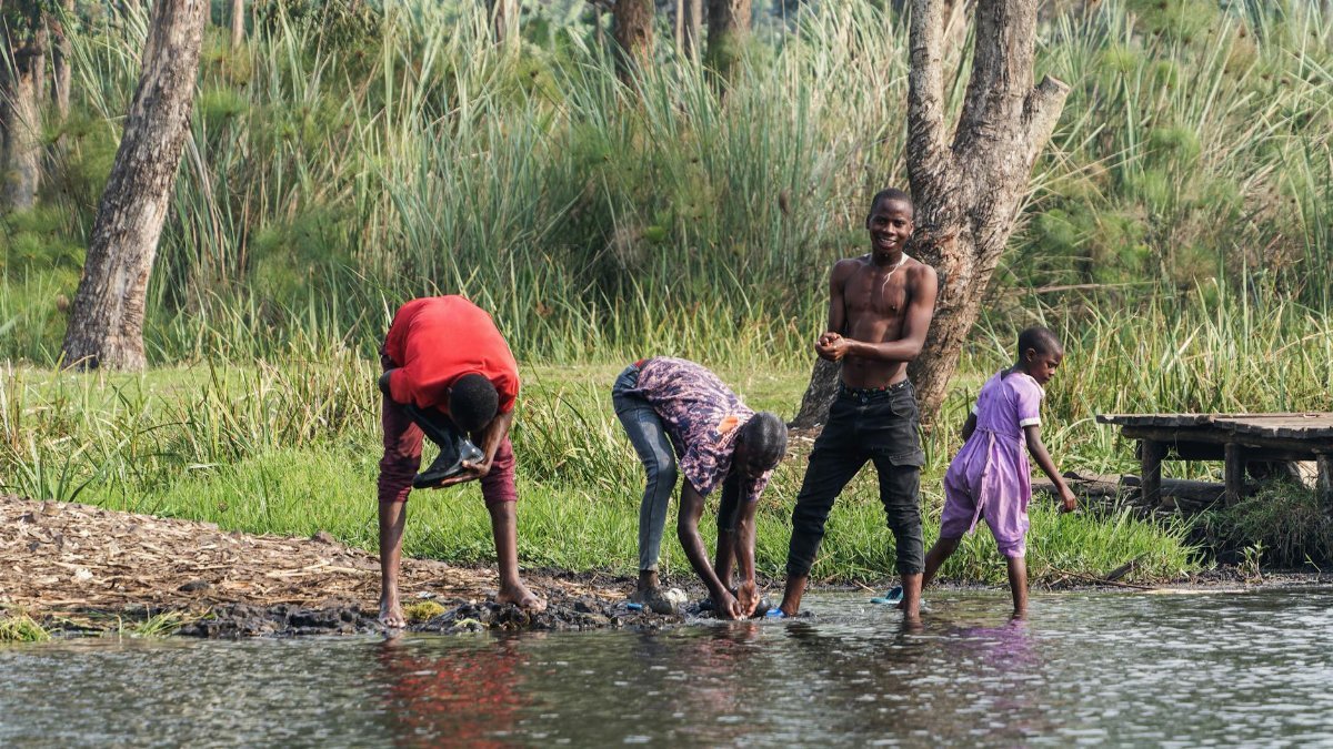 Group of people washing clothes by a serene lake in a natural setting.