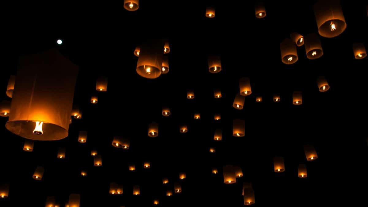 Sky lanterns float against a dark night sky during a traditional festival in Thailand.