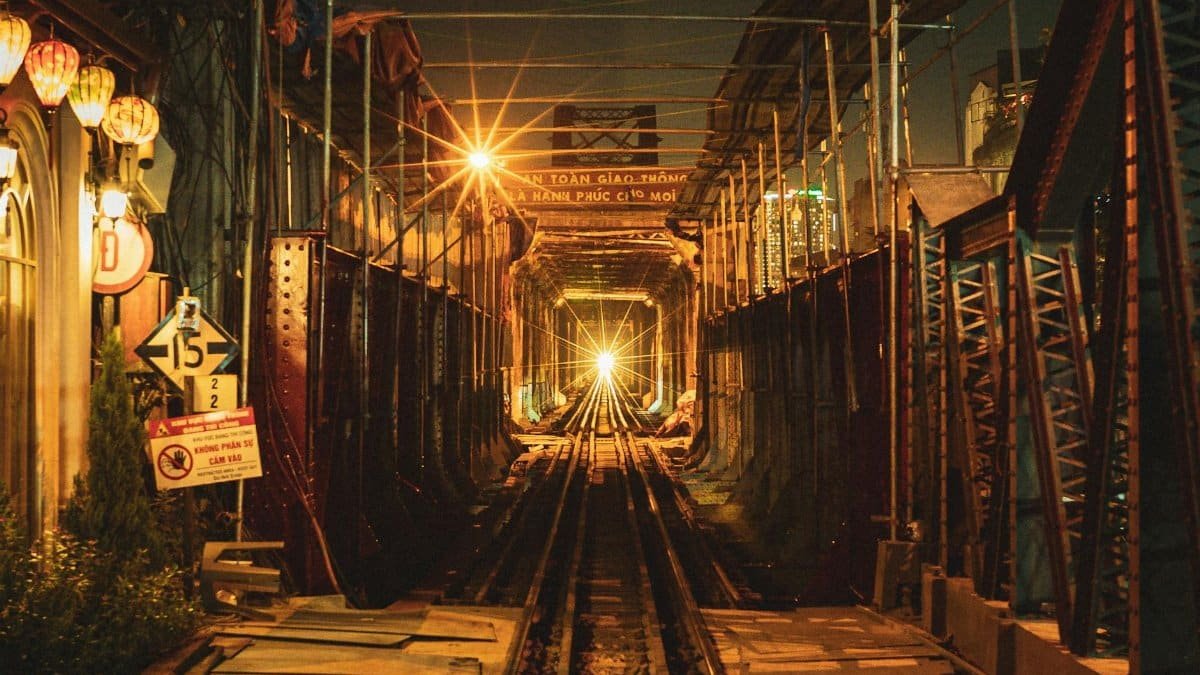 A night view of Long Bien Bridge in Hanoi, Vietnam, featuring bright lighting and a train approaching.