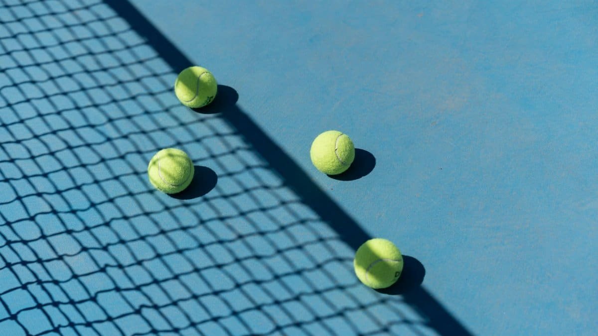 Four tennis balls resting on a blue tennis court with shadows from a net.