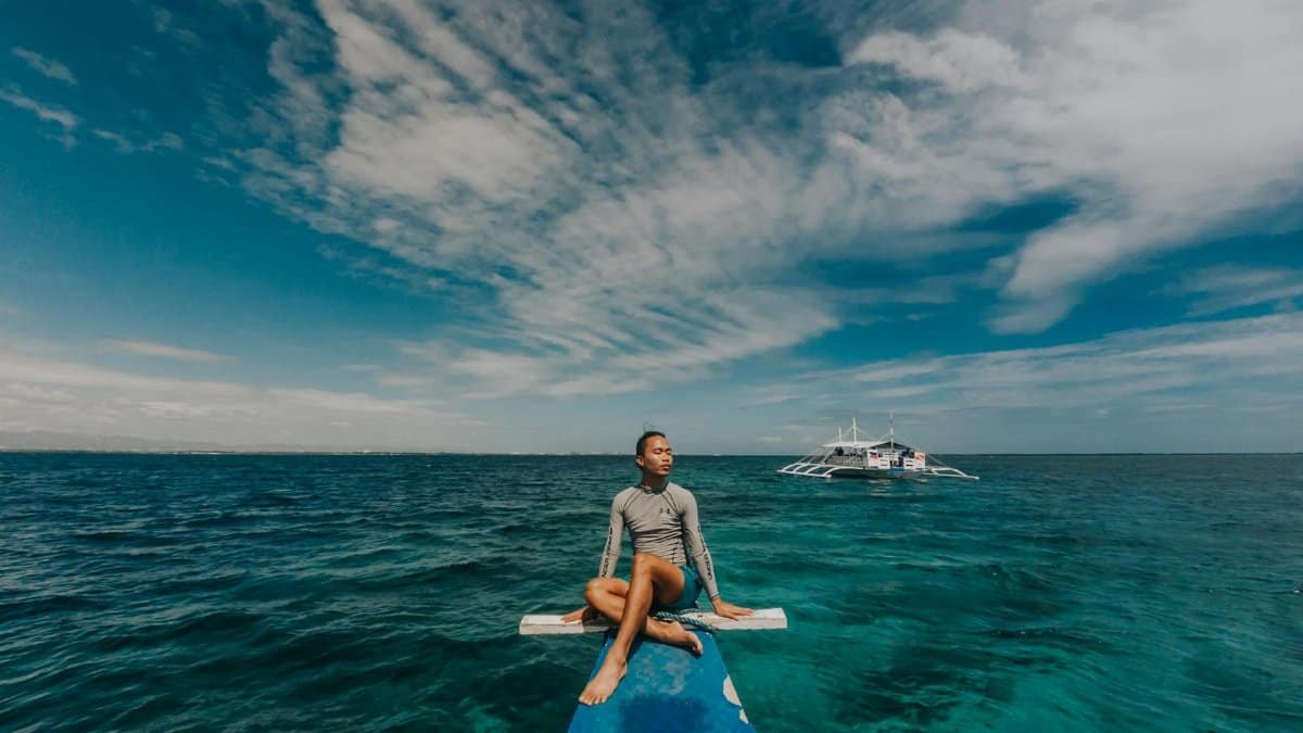 Man sitting on a boat's bow, enjoying a peaceful ocean view under a blue sky.
