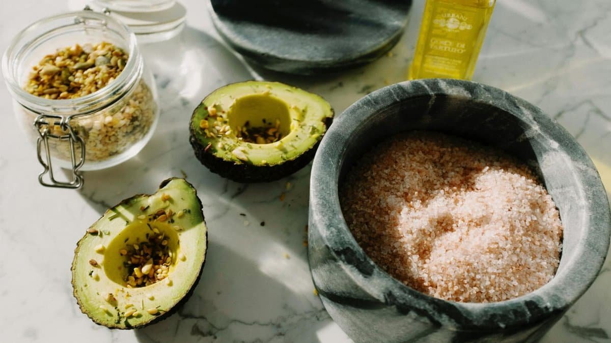 A close-up shot with avocado, pink salt, seeds, and olive oil combining for a healthy meal.