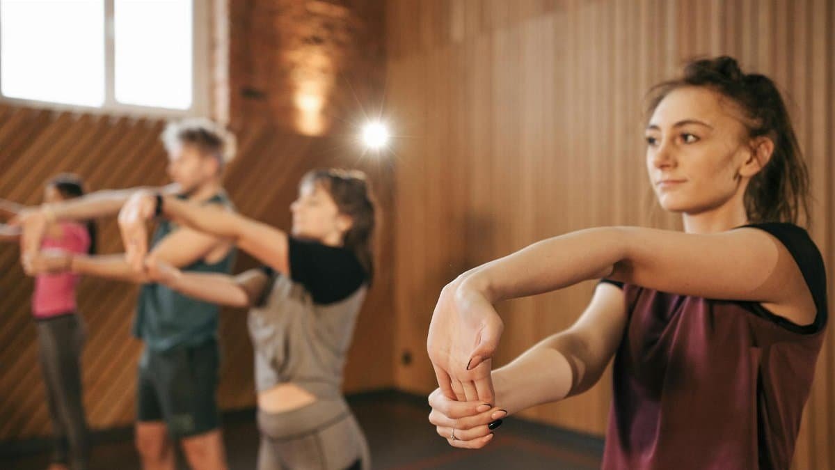 Individuals stretching during a fitness class in a gym setting, promoting group exercise.