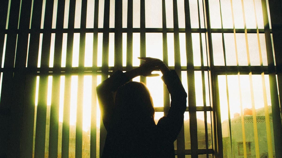 Silhouette of a woman stretching in front of large window blinds with sunlight streaming in.