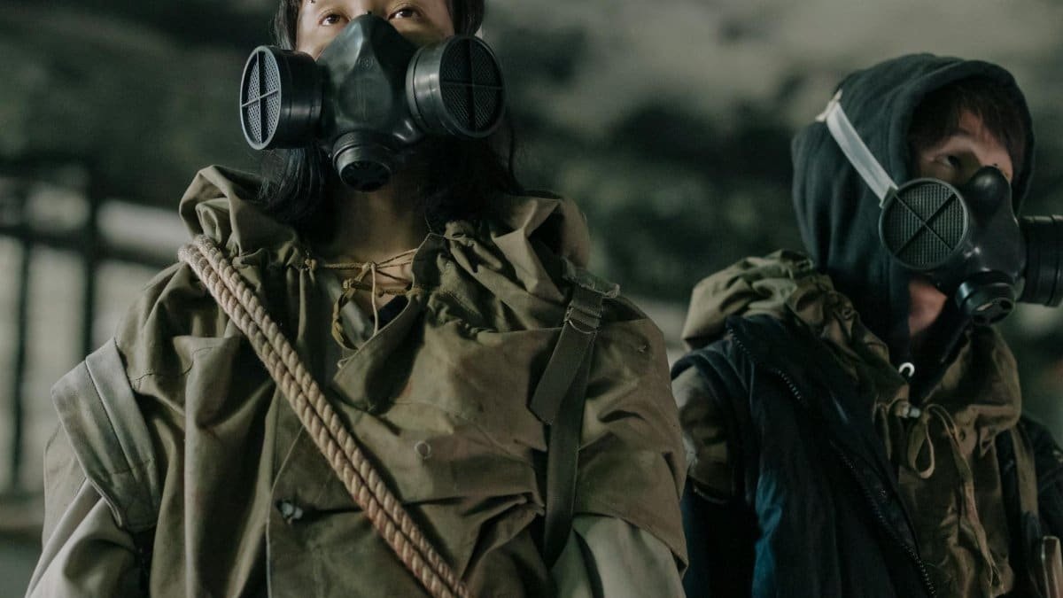 Two individuals wearing gas masks stand in a desolate, urban environment, showcasing survival and resilience.