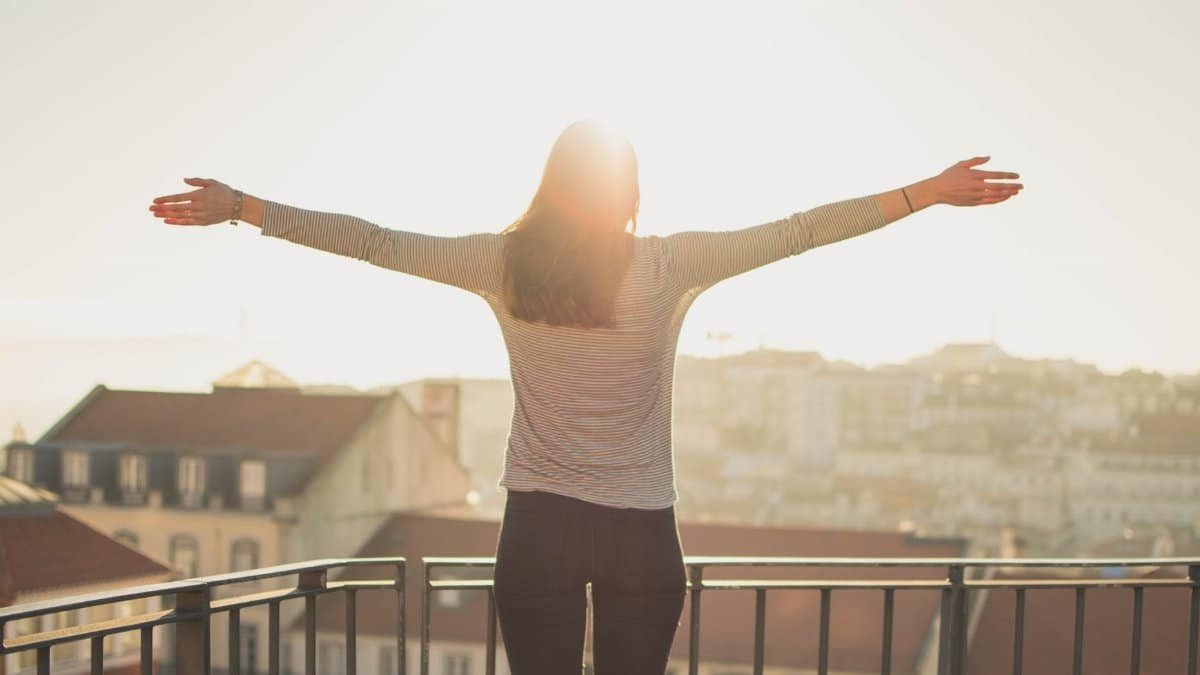 A woman stands with outstretched arms on a sunny balcony, embracing the morning light.