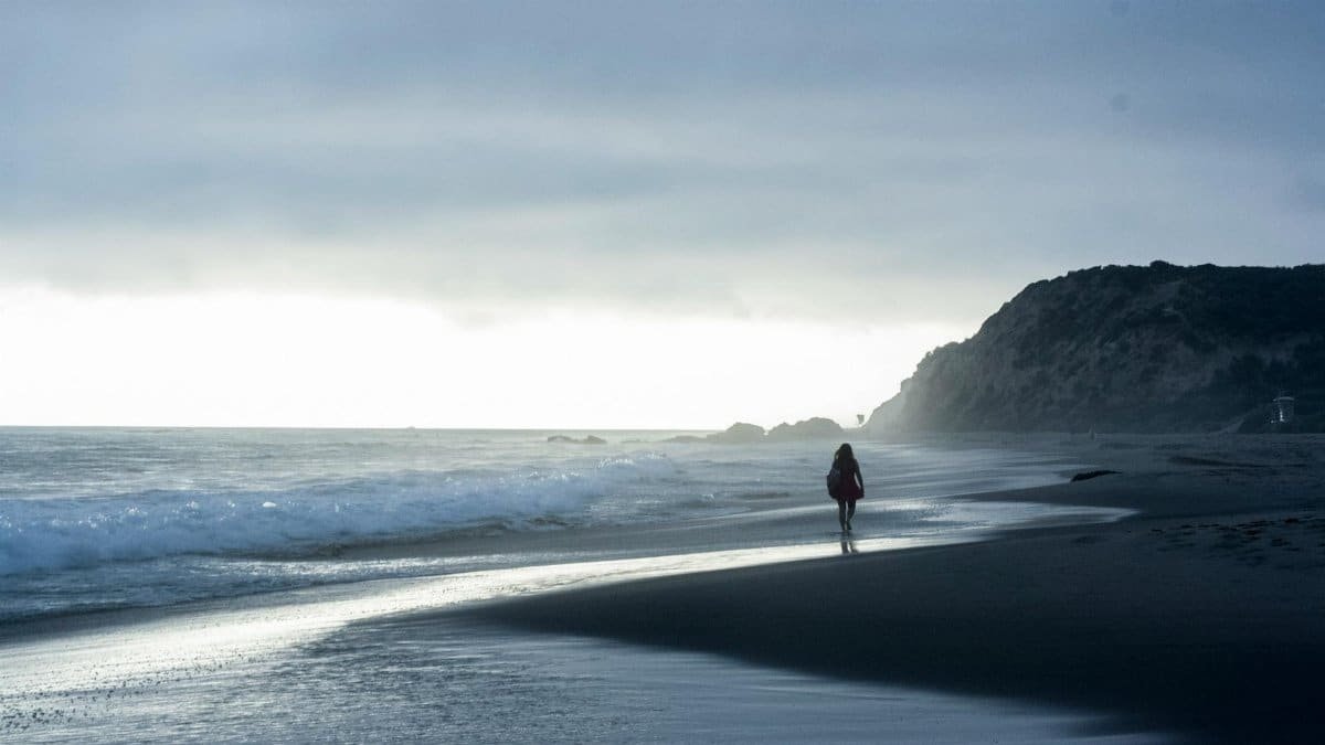 A woman walks along the calm Laguna Beach shoreline during a dramatic evening. Captivating clouds and waves.