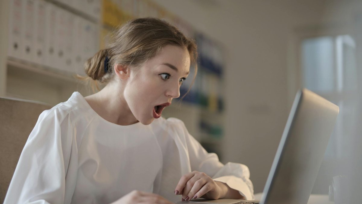 Surprised woman sitting at desk with laptop indoors, expressing amazement.