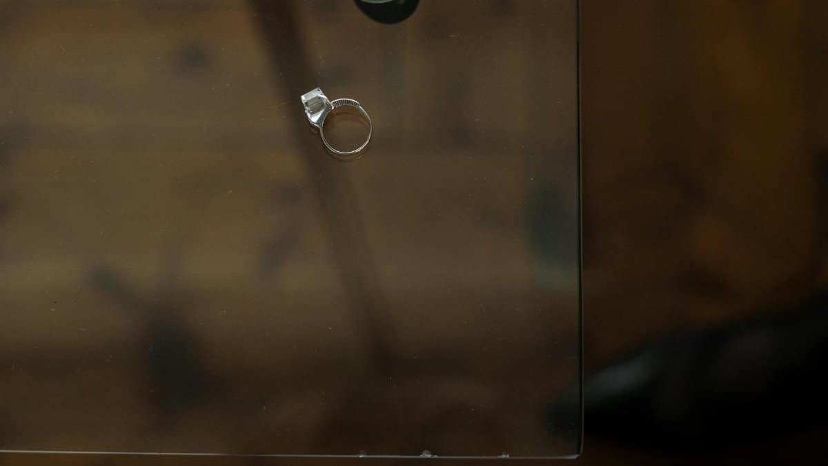 A single engagement ring rests on a glass table, symbolizing relationship reflection.