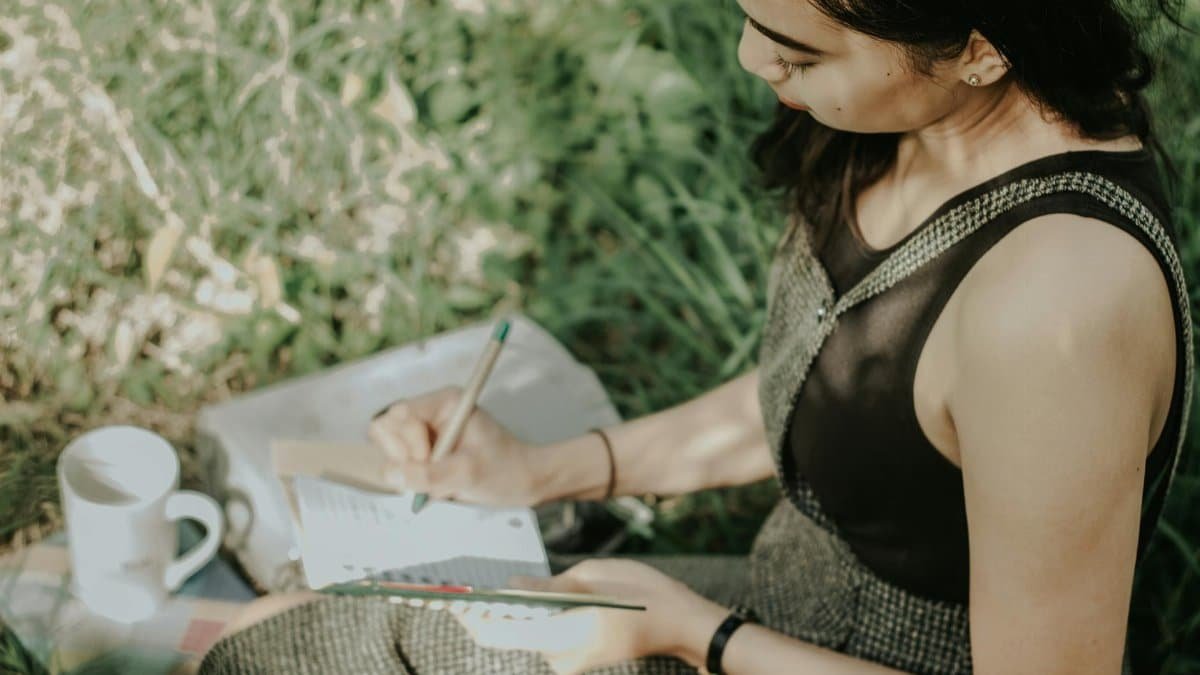 Young woman journaling outdoors, enjoying a peaceful moment with nature, pen in hand.