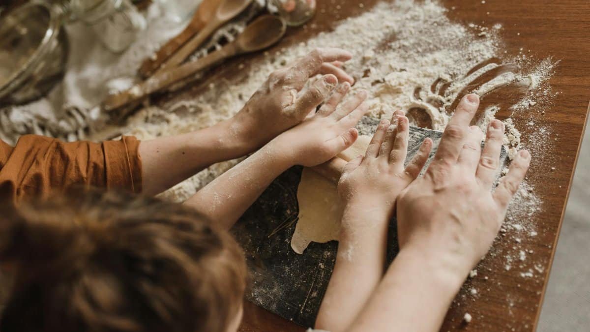 A parent and child bonding while kneading dough in a messy kitchen environment.