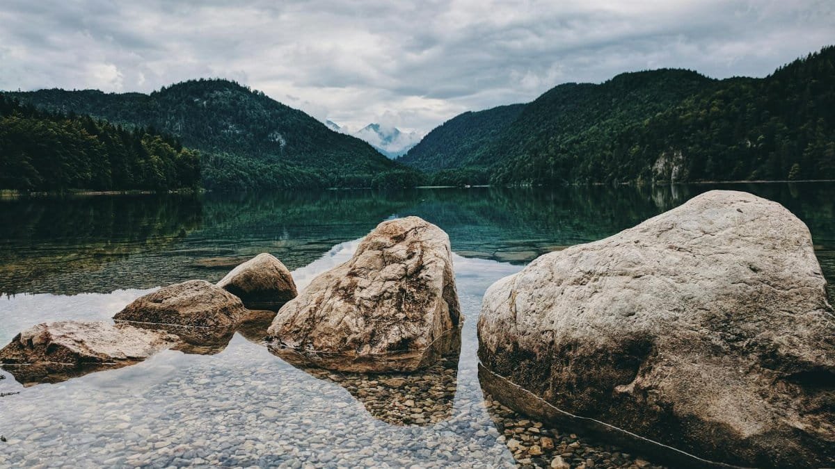 Peaceful lake in Schwangau, Germany, surrounded by scenic mountains and rocks, capturing nature's serenity.