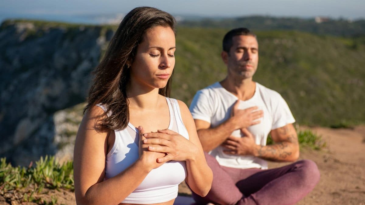 Two adults meditating outdoors in Portugal, embracing a serene yoga practice under the sun.