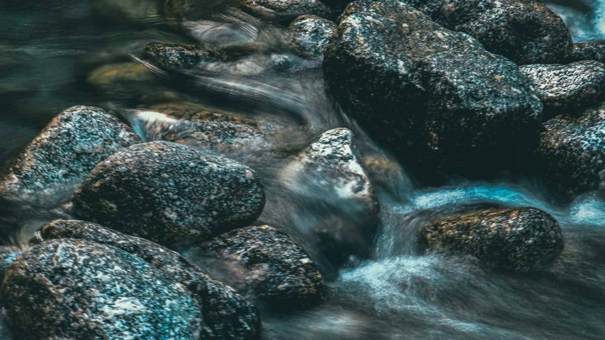 Scenic view of shallow river with rapid water fluid between big stones with spots in daylight