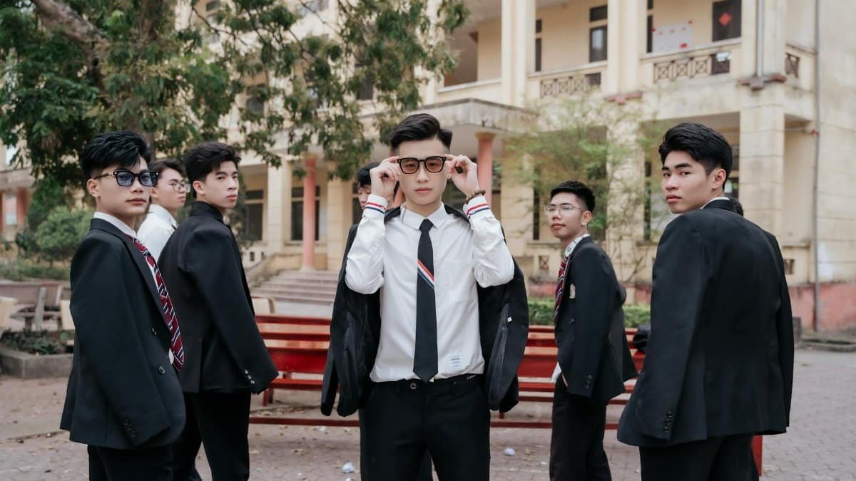 Six young men in formal suits and ties posing confidently outdoors.