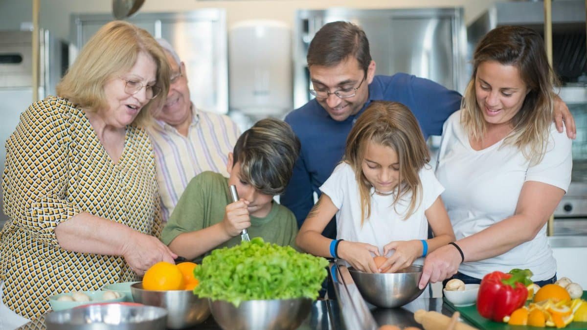 Family of various ages gathers in kitchen to cook meal together, showcasing culinary togetherness.