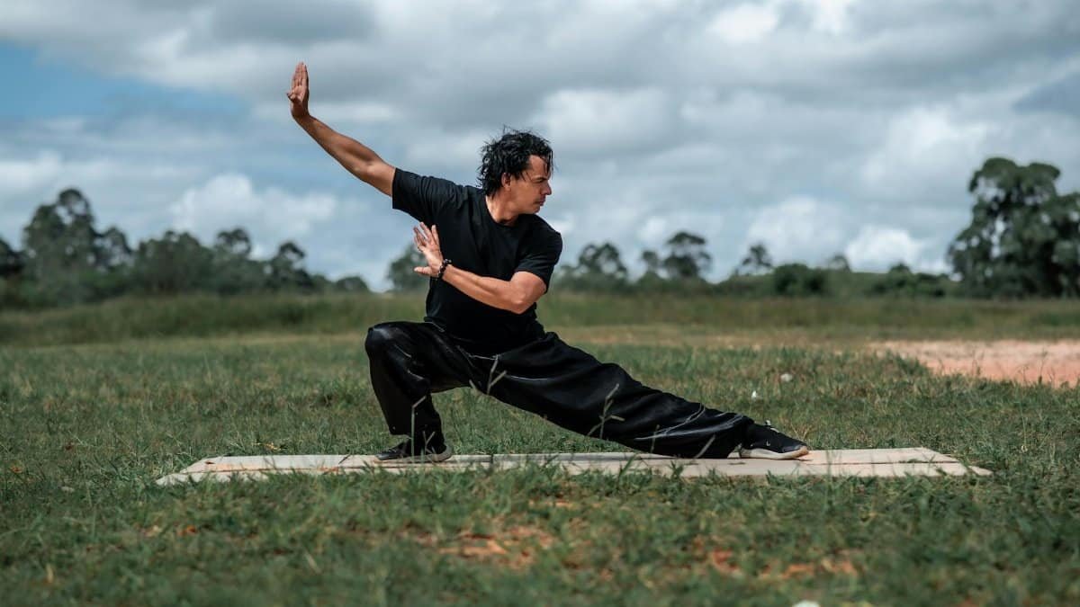 Adult man performing Tai Chi on a grassy field, showcasing martial arts mindfulness in nature.