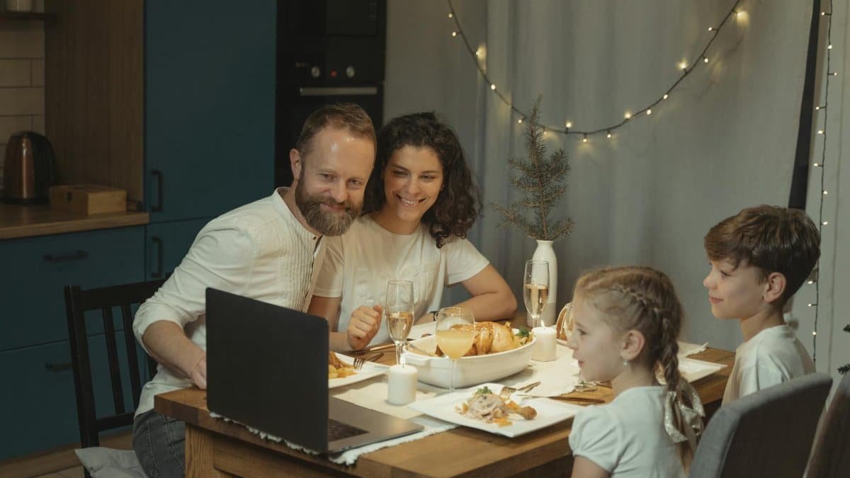 Family enjoying a Christmas dinner with online video call, sharing holiday joy indoors.