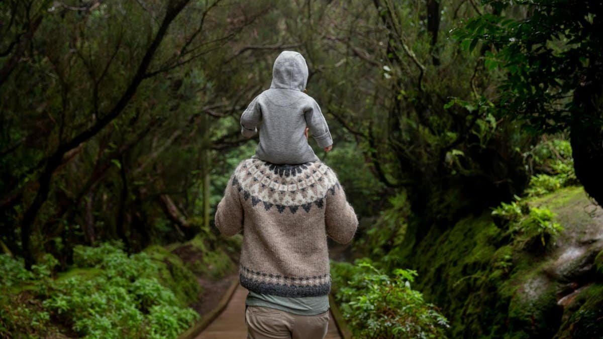 A father carrying his child on a forest path, enjoying nature and bonding on an autumn day.